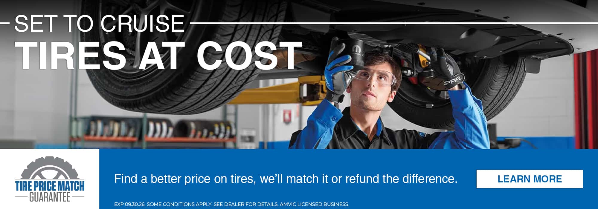 Mechanic inspecting tire under vehicle with "Tires at Cost" offer and price match guarantee.