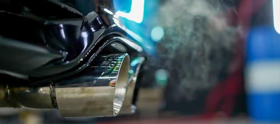 Car exhaust pipe emitting smoke, highlighting vehicle emissions and environmental impact.