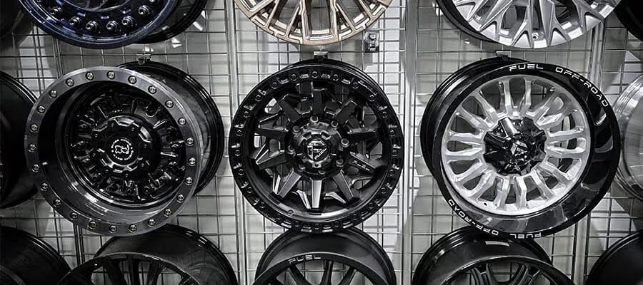 Display of various alloy wheels on a metal grid wall, featuring intricate designs and multiple finishes.
