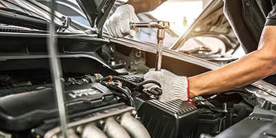 Mechanic wearing gloves using a wrench to repair a car engine in a well-lit garage.