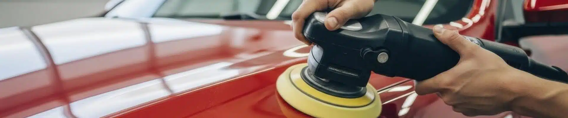 Polishing a red car with an electric buffer, enhancing the shine of the paintwork.