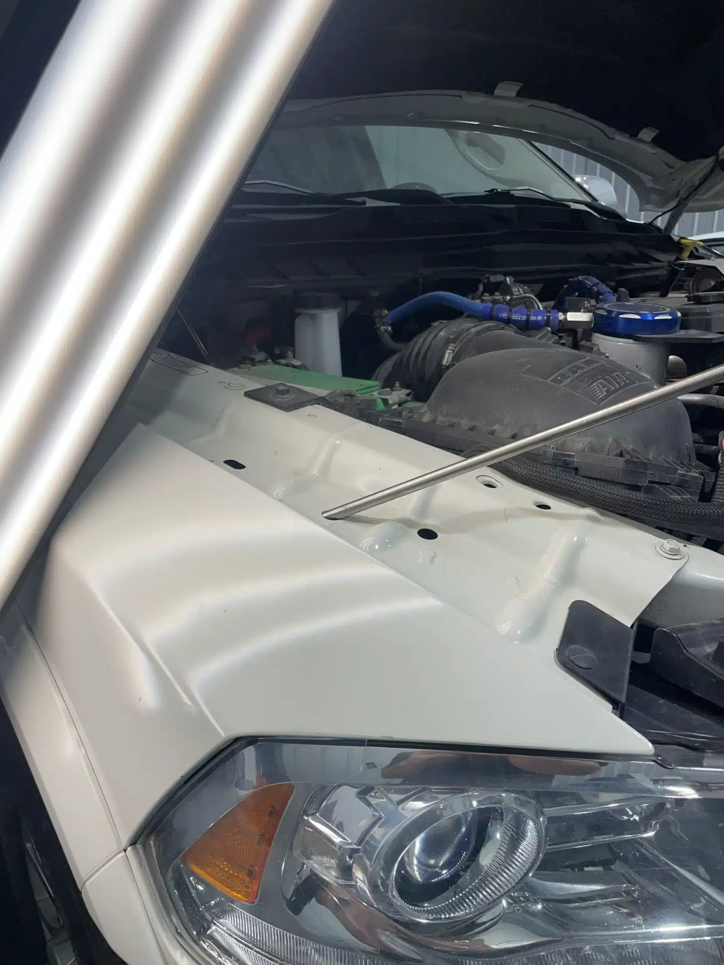 Car hood open, showing engine and headlight details inside a garage.